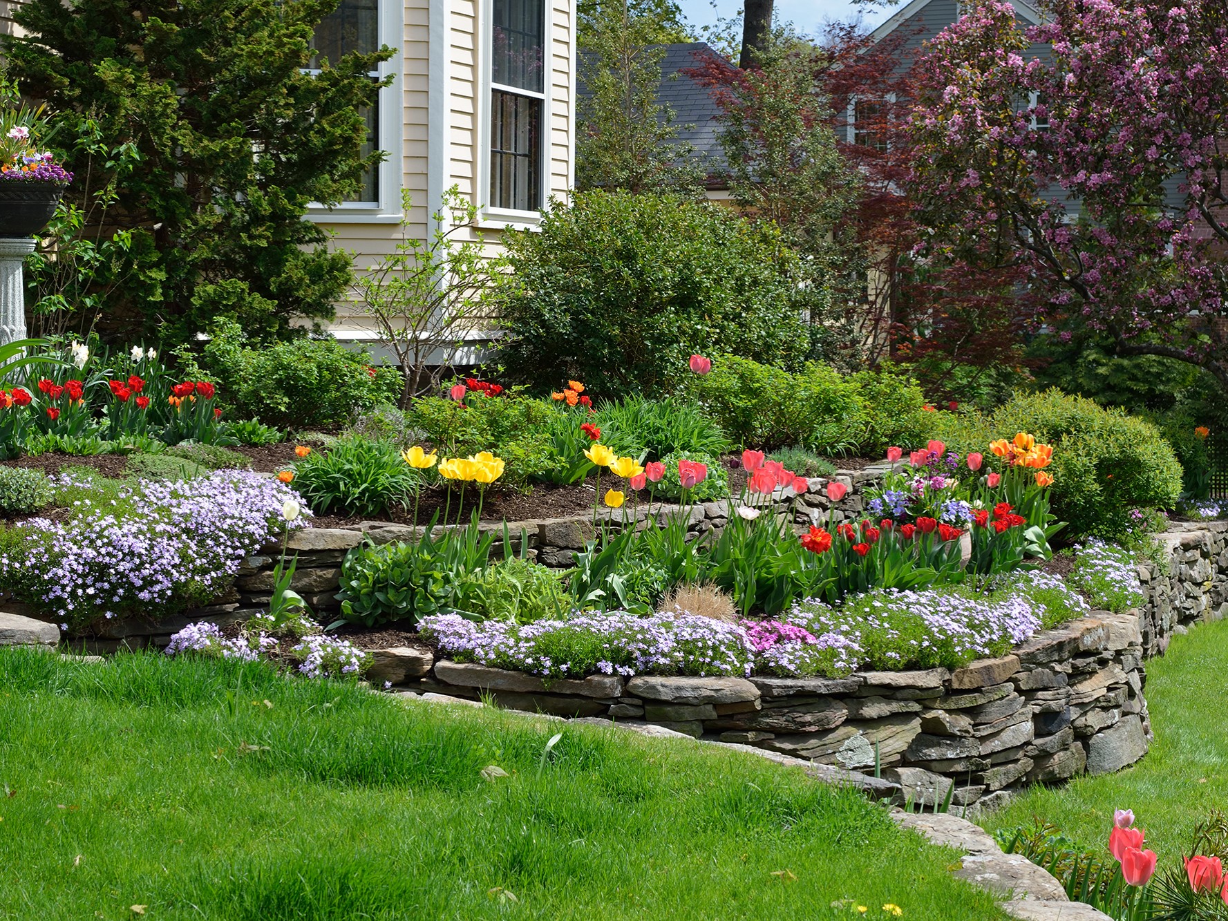 multi-layer paver stone retaining wall filled with fresh flowers and mulch. hardscaping service by bret-mar