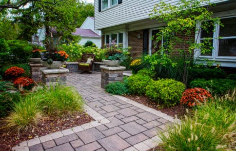 winding paver stone walkway leading to brick paver retaining wall and brick pillars. Brick pavers surrounded by fresh mulch and plants