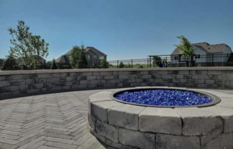 brick fire pit with glass rocks on brick paver patio with brick retaining wall surrounding. Hardscaping services by bret-mar