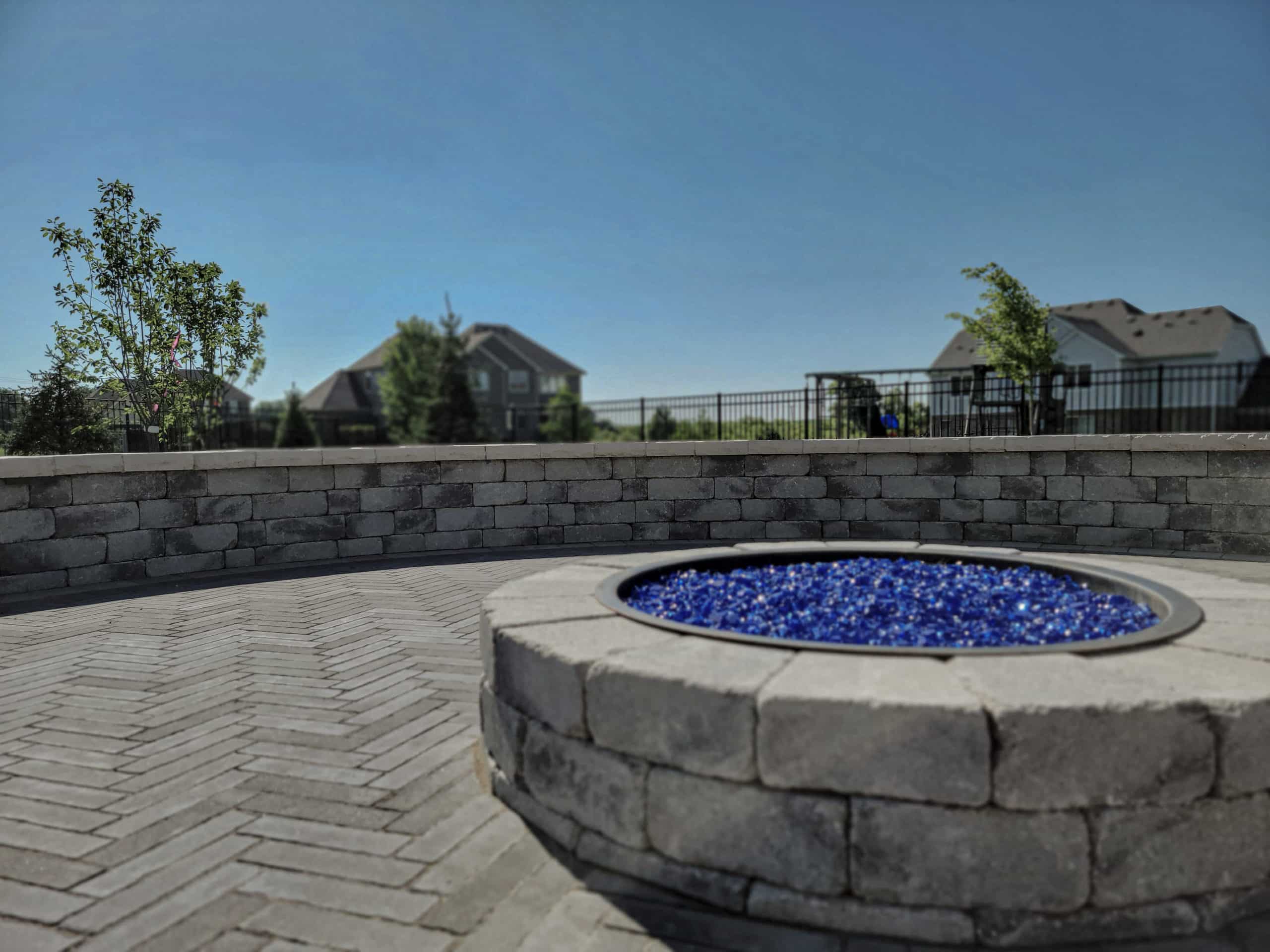 brick fire pit with glass rocks on brick paver patio with brick retaining wall surrounding. Hardscaping services by bret-mar