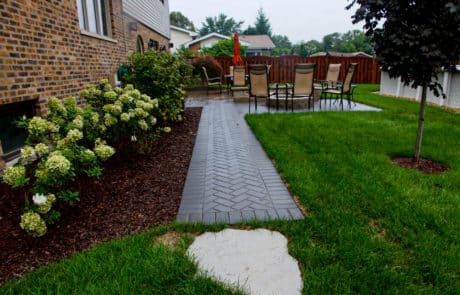 fresh hardscaping of brick paver patio and brick paver walkway in backyard. Fresh landscaping of mulch and flowers in background