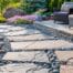 in a sophisticated urban garden setting, carefully designed hardscapes seamlessly blend with vibrant garden elements, showcasing a stylish stone pathway winding through manicured flower beds, a modern terrace adorned with sleek outdoor furniture, and decorative gravel accents that add texture, all illuminated by bright, soft daylight that highlights the intricate details of each element. the scene captures a sense of harmony, blending the rigidity of hardscape materials like stone and concrete with the organic beauty of blooming flowers and foliage, reflecting the essential steps for integrating hardscape into residential gardens. the composition features a wide-angle perspective, showcasing a beautifully arranged layout that invites viewers to explore the space. a color palette consisting of warm neutrals and rich greens, with pops of colorful blooms, enhances the vibrancy and liveliness of the setting. shot with a canon eos r5 using a rf 15-35mm f/2.8 l is usm lens, the image employs ai-driven autofocus to ensure clarity and detail in every aspect of the scene. natural light flows from the left, creating a subtle contrast and depth, while a minimalist, photorealistic artistic style captures the realism of the materials and the harmony of design principles, illustrating the ideals of blending hardscape into a garden environment.