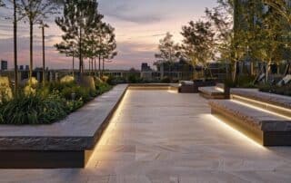 a meticulously designed urban hardscape unveils a striking interplay of textured stone pathways, sleek concrete seating areas, and innovative lighting arrangements, all set against a modern cityscape backdrop.