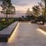 a meticulously designed urban hardscape unveils a striking interplay of textured stone pathways, sleek concrete seating areas, and innovative lighting arrangements, all set against a modern cityscape backdrop.