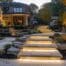 a sophisticated outdoor living space featuring expertly arranged stone pathways, elegant patios, and meticulously designed hardscape elements, all illuminated by warm, ambient lighting in an upscale residential neighborhood.